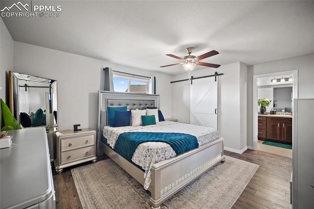 Bedroom featuring a barn door, dark wood-type flooring, a ceiling fan, and connected bathroom