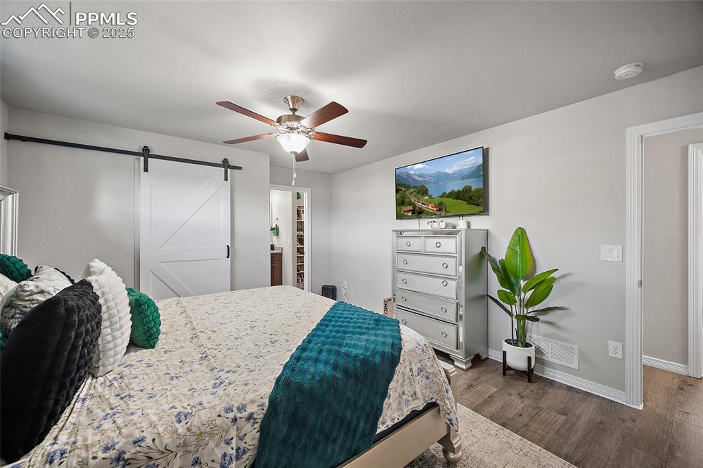 Bedroom with a barn door, dark wood-style flooring, ceiling fan, and a spacious closet