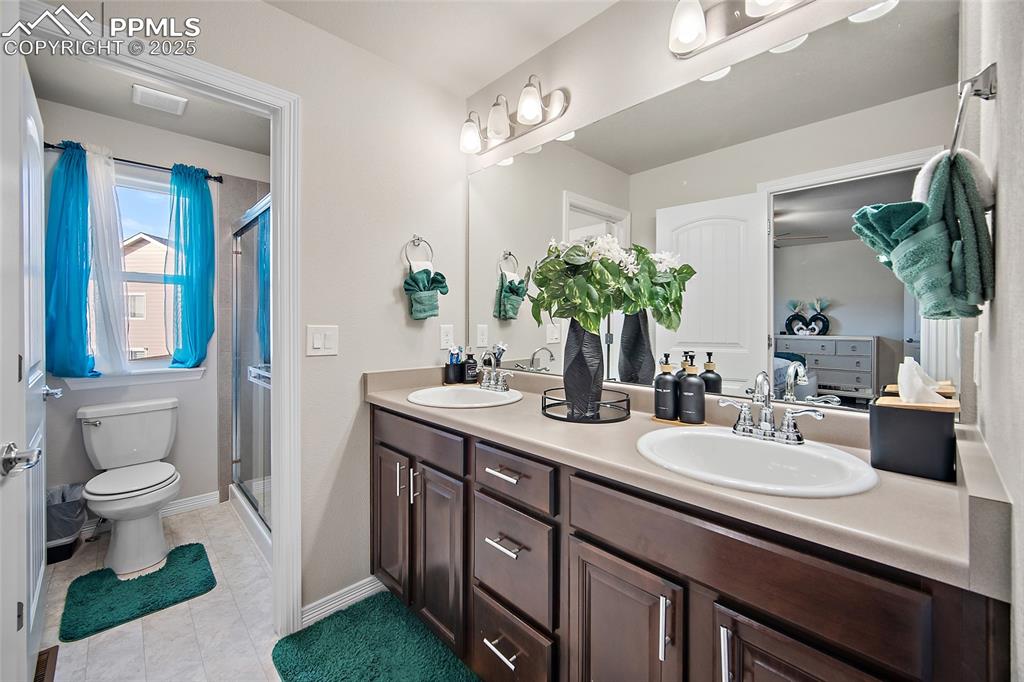 Ensuite bathroom featuring double vanity, a stall shower, and light tile patterned flooring