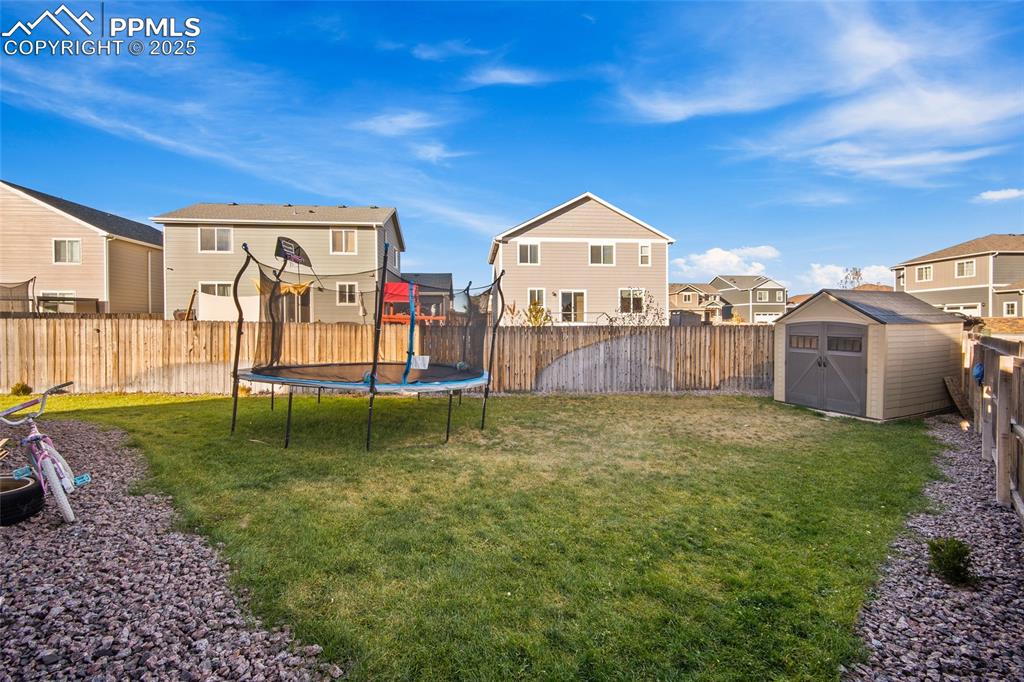 Fenced backyard featuring a residential view, a storage unit, and a trampoline
