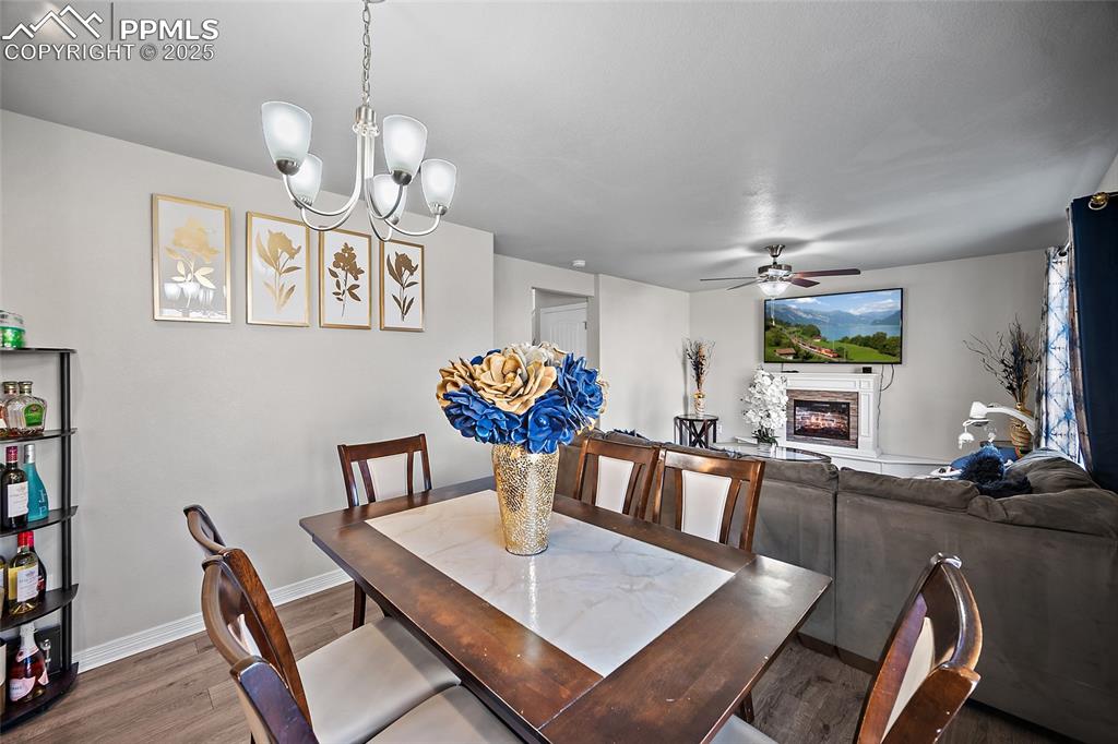 Dining space with a glass covered fireplace, wood finished floors, a chandelier, and ceiling fan