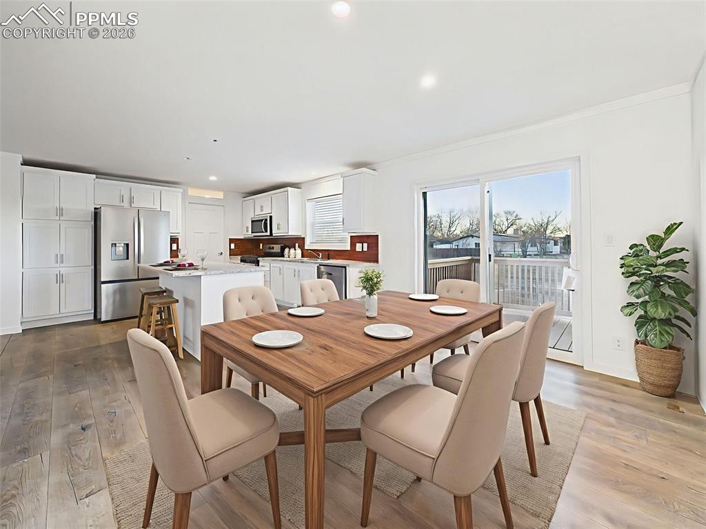 Virtually This bright, open-concept kitchen and dining space features crisp white cabinetry, stainless steel appliances, and a center island with bar seating. A sliding glass door leads directly to the back deck, perfect for indoor-outdoor dining.