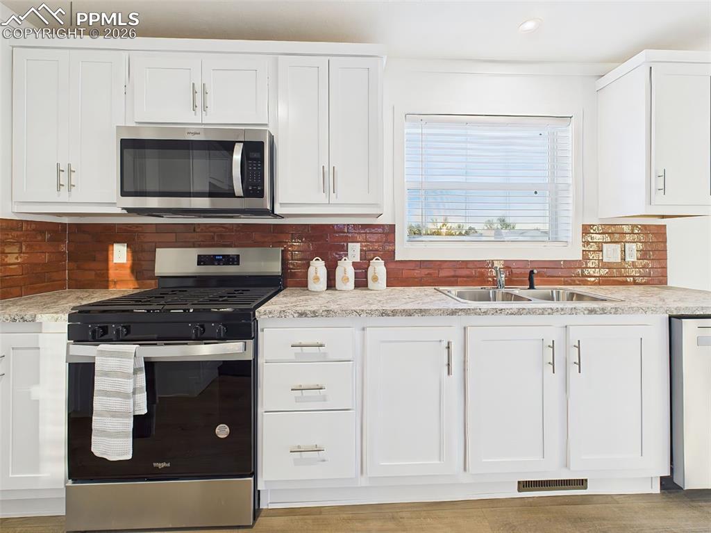 A closer look at the kitchen reveals a Whirlpool gas range, built-in microwave, and large sink beneath a picture window offering natural light.