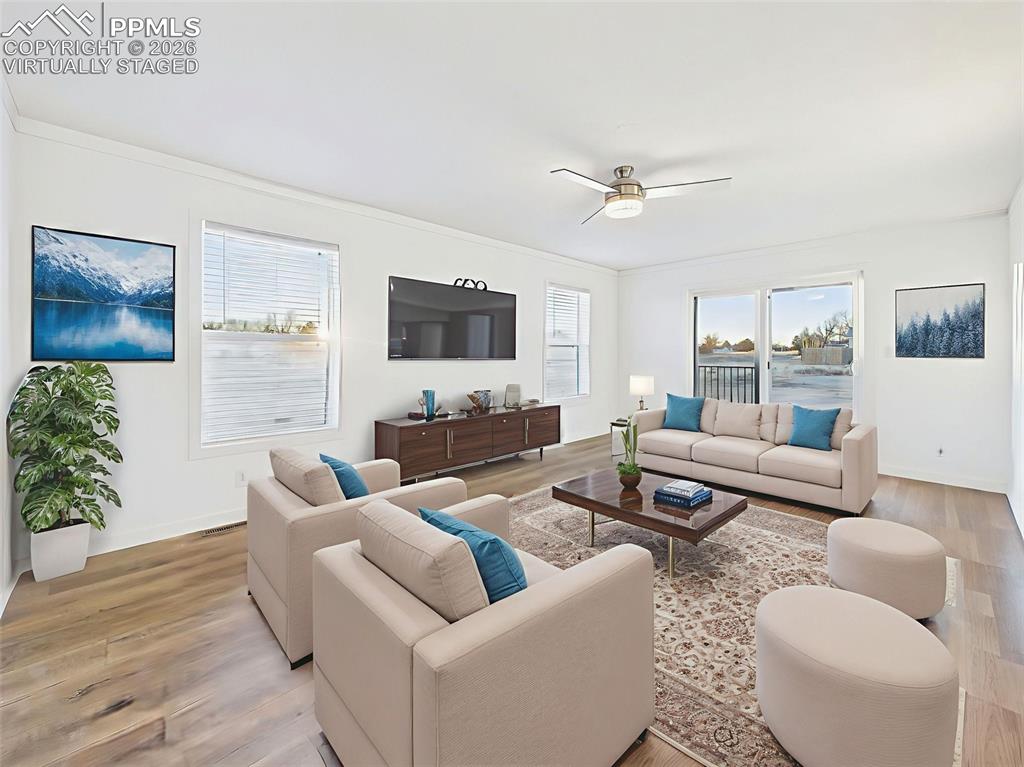 Virtually Staged A spacious and sunlit living area with large windows, modern ceiling fan, and seamless access to the backyard through sliding glass doors—ideal for gathering or relaxing.
