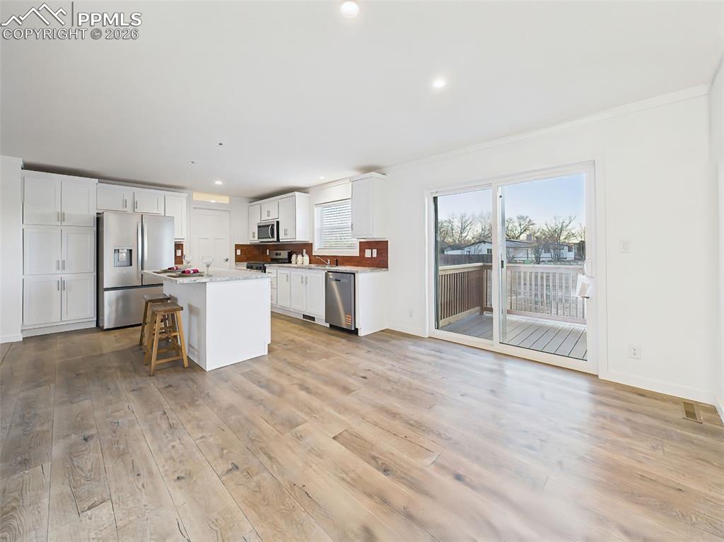 Natural light fills the kitchen and dining area, highlighting the warm wood floors, sleek finishes, and functional layout that flows effortlessly to the outdoor deck.