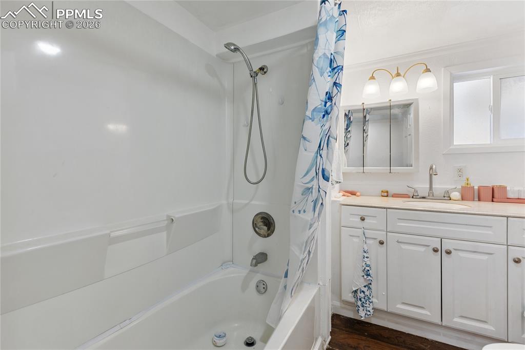 The bathroom featuring shower / bathtub combination with curtain, vanity, and dark wood finished floors