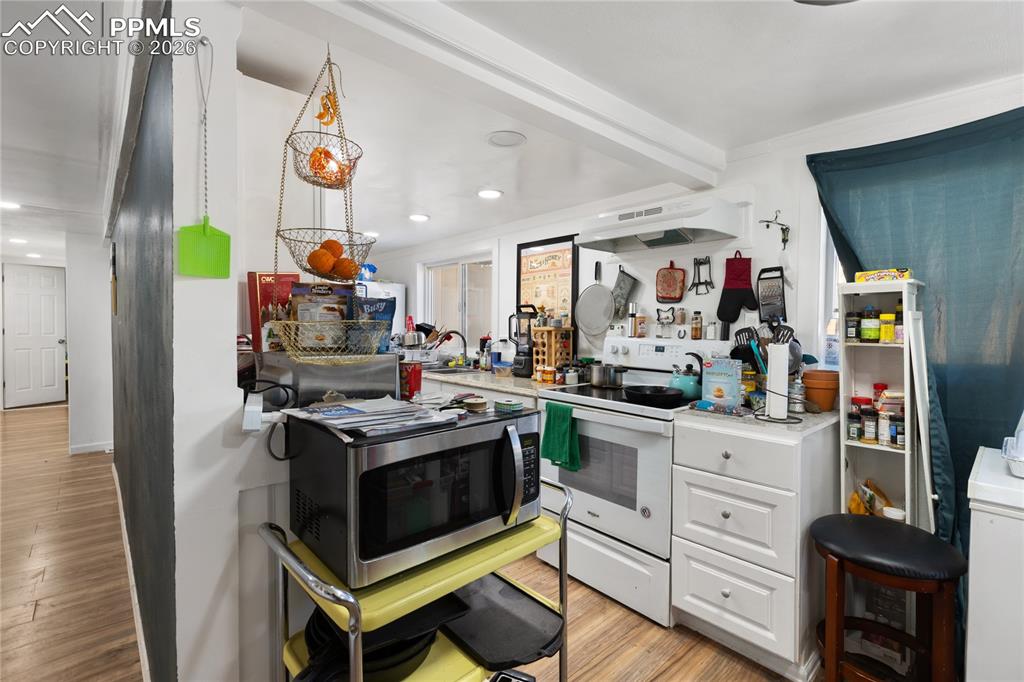 The kitchen with light wood-style floors, white electric range, stainless steel microwave, white cabinets, and crown molding!