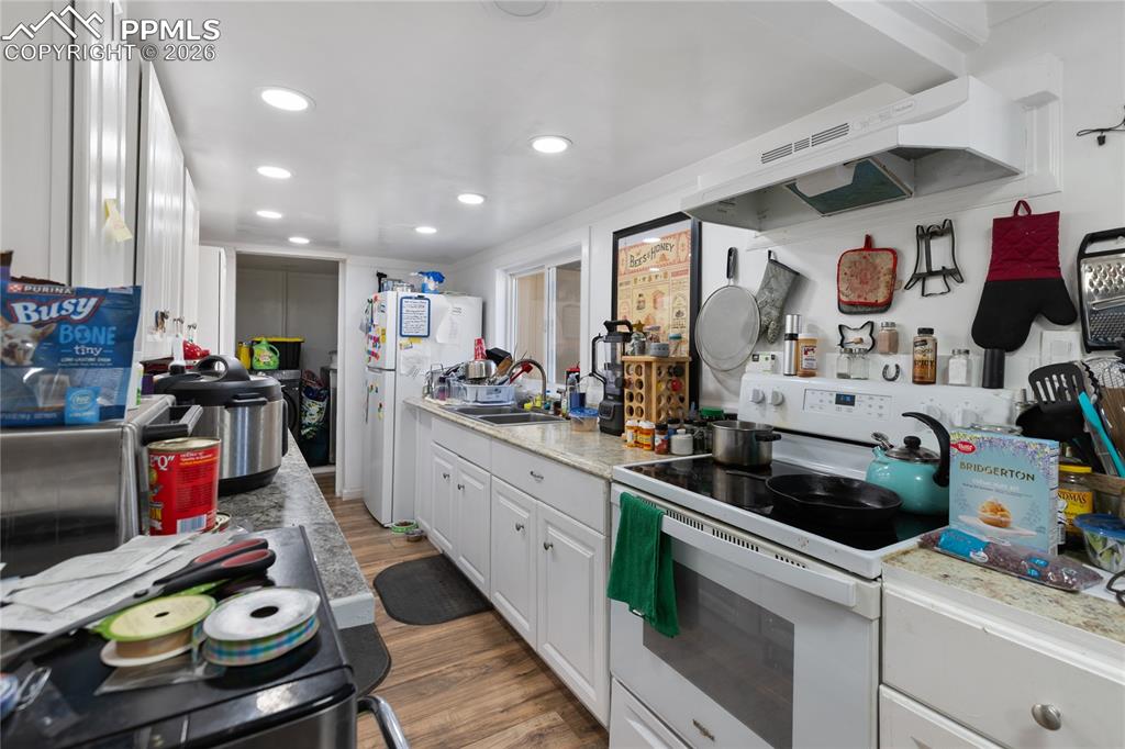 Kitchen with white appliances, white cabinets, light countertops, light wood-style floors, and recessed lighting