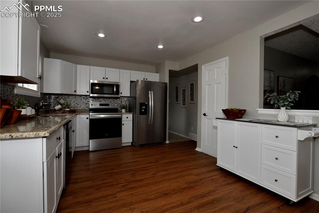 Kitchen with appliances with stainless steel finishes, decorative backsplash, dark wood-type flooring, white cabinets, and recessed lighting