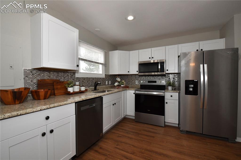 Kitchen featuring appliances with stainless steel finishes, dark wood-type flooring, white cabinets, backsplash, and recessed lighting