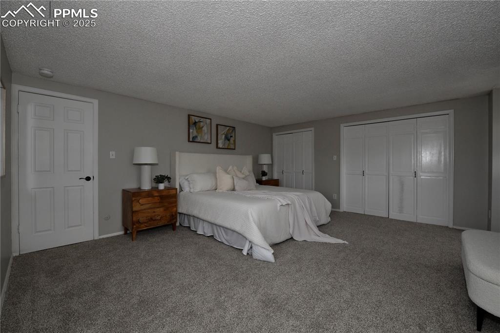 Carpeted bedroom featuring a textured ceiling and multiple closets