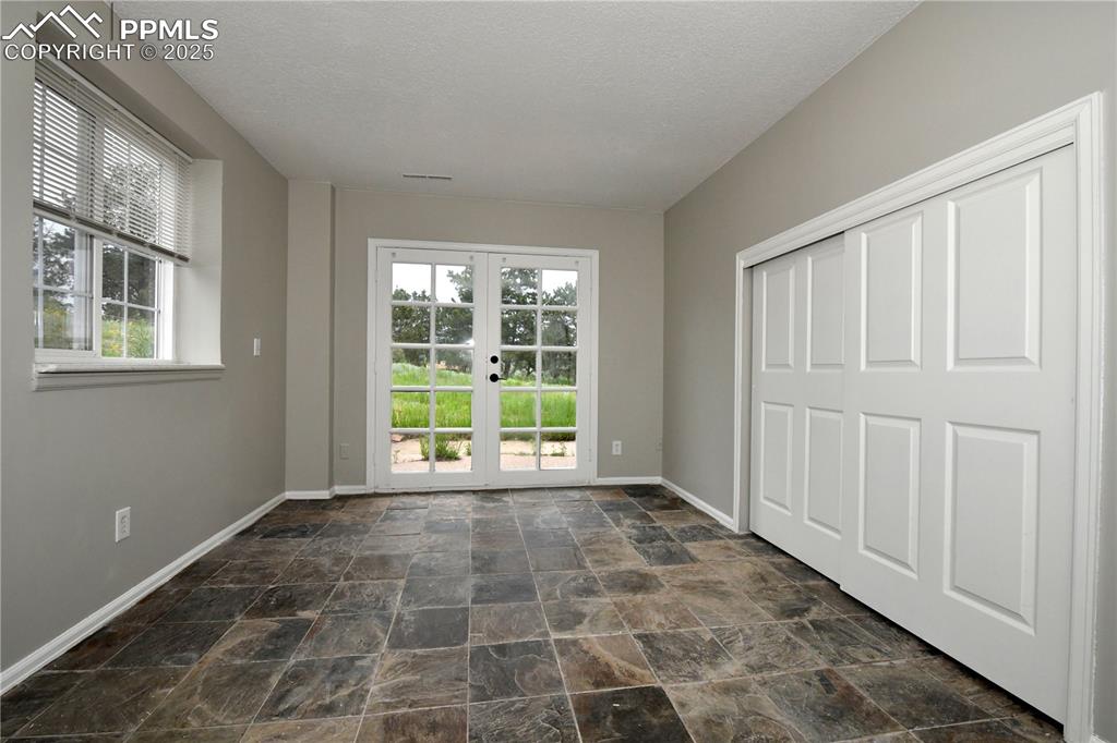 Unfurnished bedroom featuring baseboards, dark stone finish flooring, french doors, access to outside, and a textured ceiling