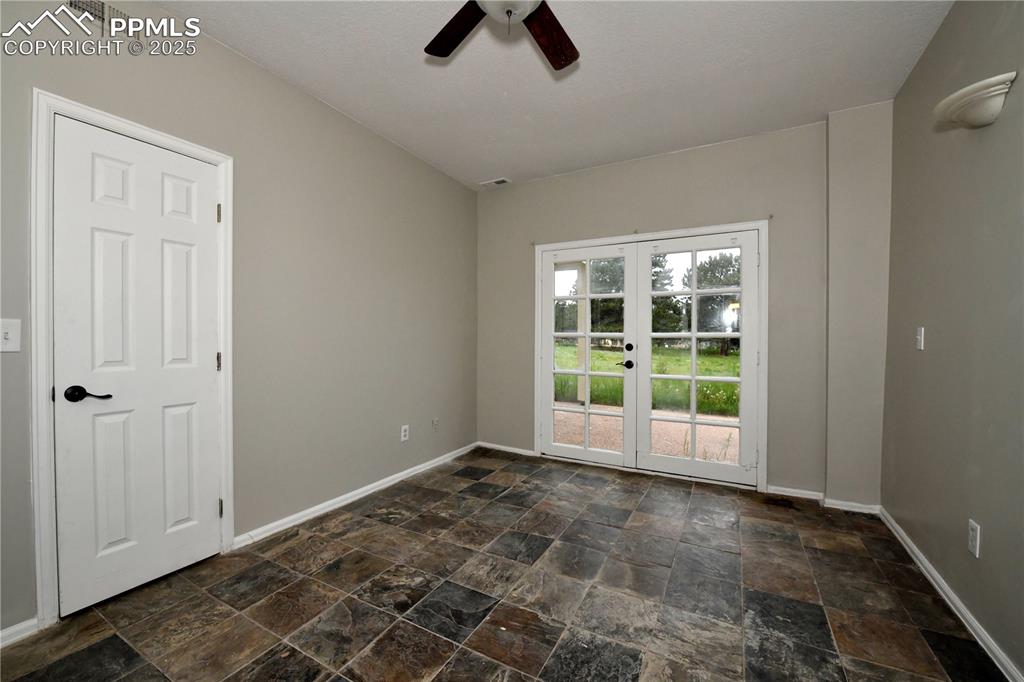 Unfurnished room featuring french doors, stone tile floors, ceiling fan, and baseboards