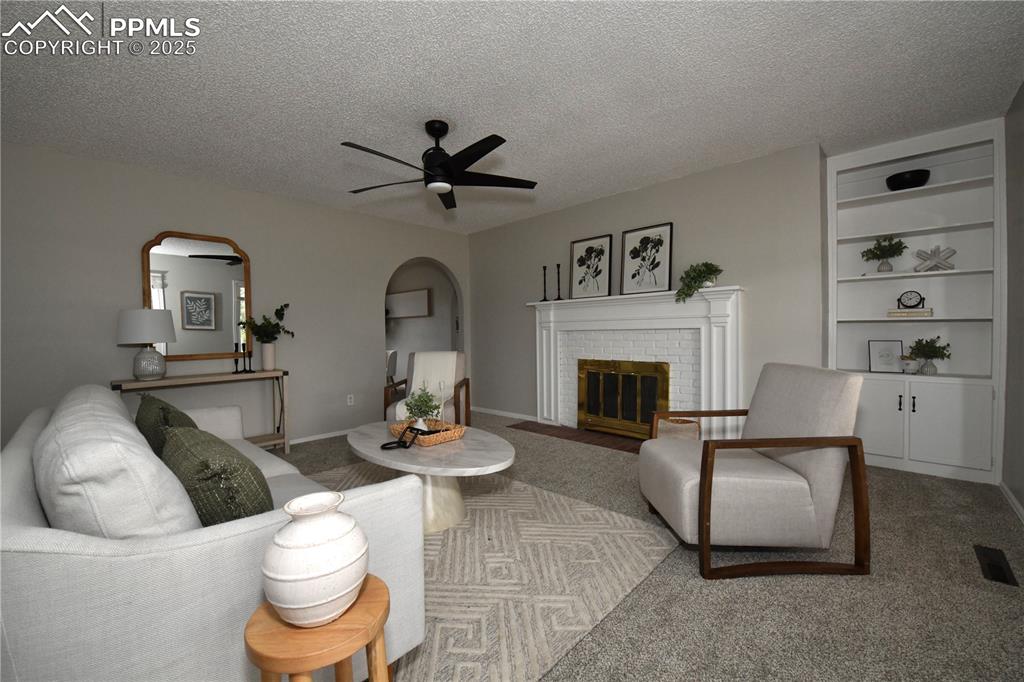 Carpeted living room with arched walkways, a textured ceiling, a ceiling fan, and a brick fireplace