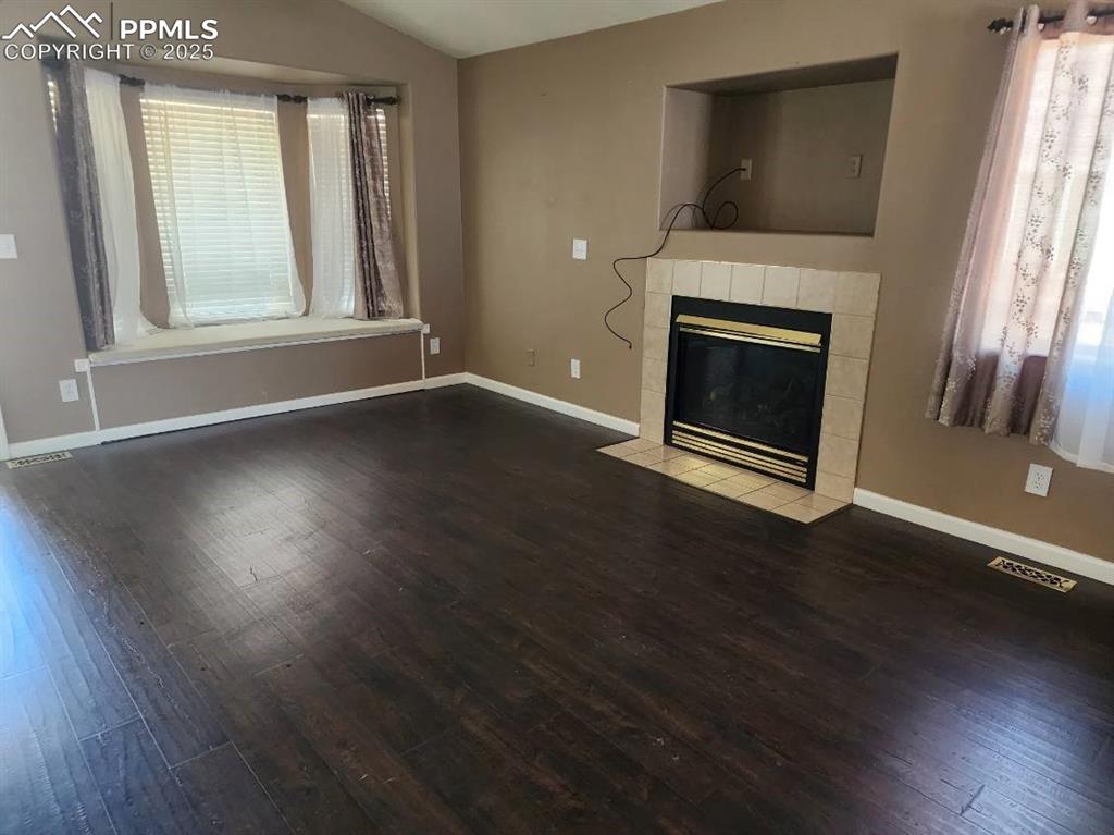 Unfurnished living room featuring lofted ceiling, dark wood-style flooring, and a tile fireplace