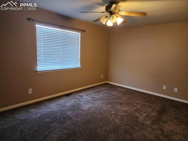 Empty room with dark colored carpet and a ceiling fan