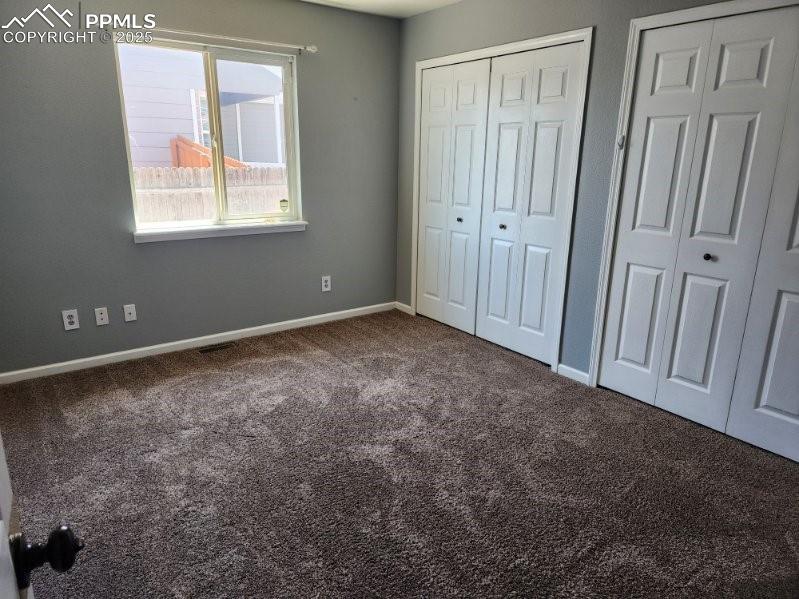 Unfurnished bedroom with two closets and dark carpet