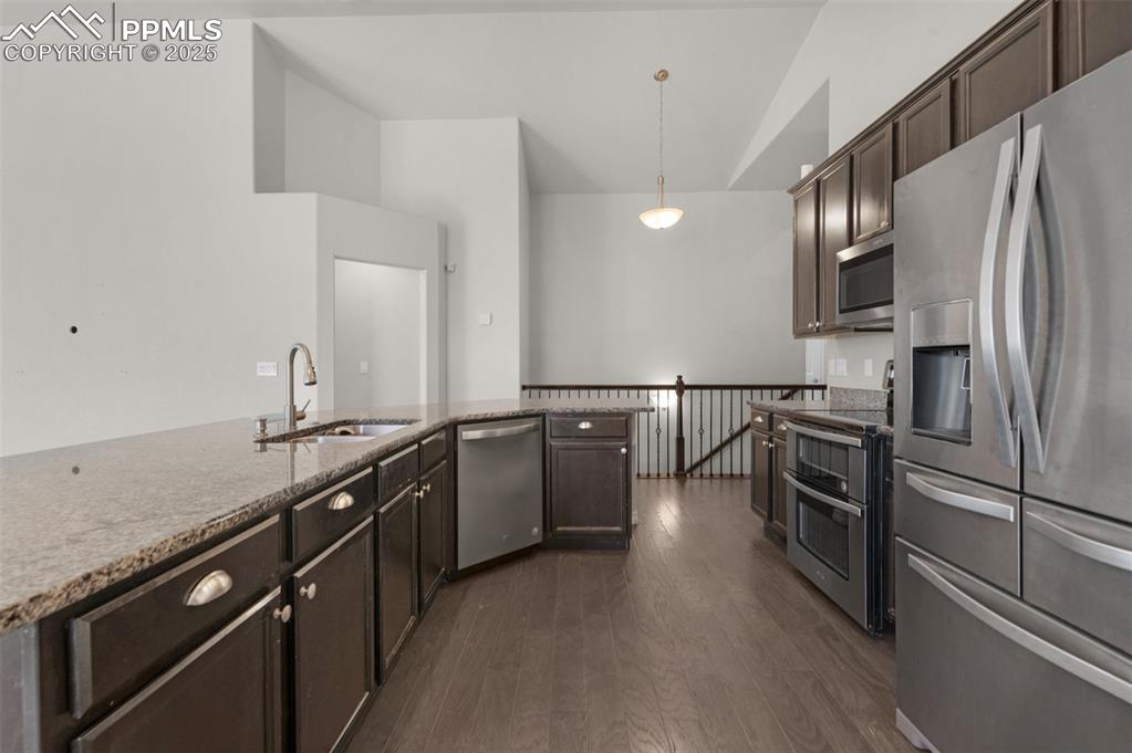 Kitchen featuring stainless steel appliances, dark brown cabinetry, dark wood-style flooring, light stone counters, and lofted ceiling