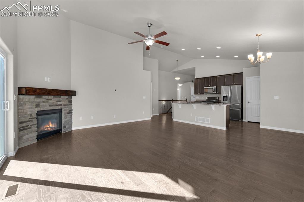 Living area with cozy fireplace, ceiling fan, high vaulted ceiling, and wood finished floors