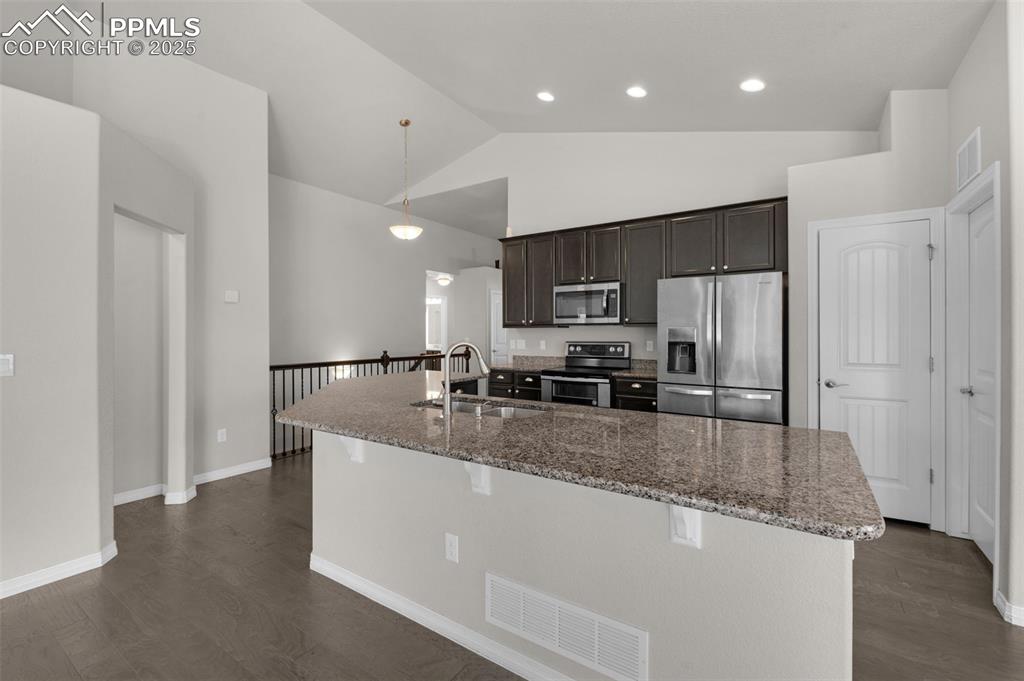 Kitchen with stainless steel appliances, stone counters, dark wood finished floors, high vaulted ceiling, and recessed lighting