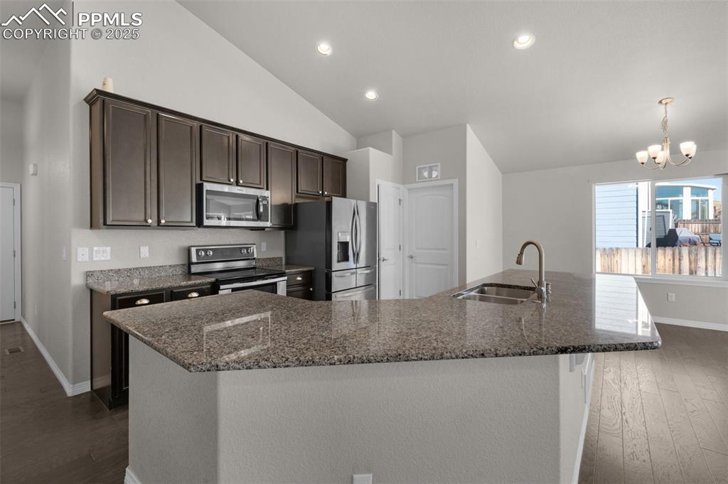 Kitchen with dark brown cabinetry, appliances with stainless steel finishes, a large island, recessed lighting, and dark stone countertops