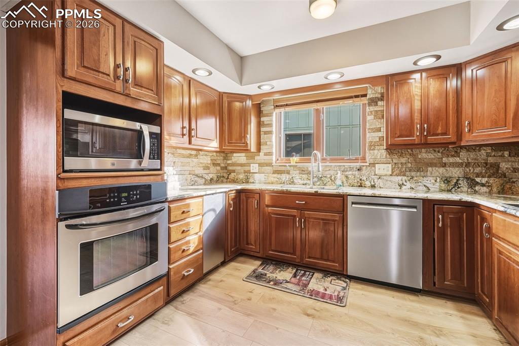 Bright and functional kitchen featuring abundant cabinetry, stainless steel range and microwave, dishwasher, and a window above the sink bringing in natural light. Durable updated flooring completes the space.