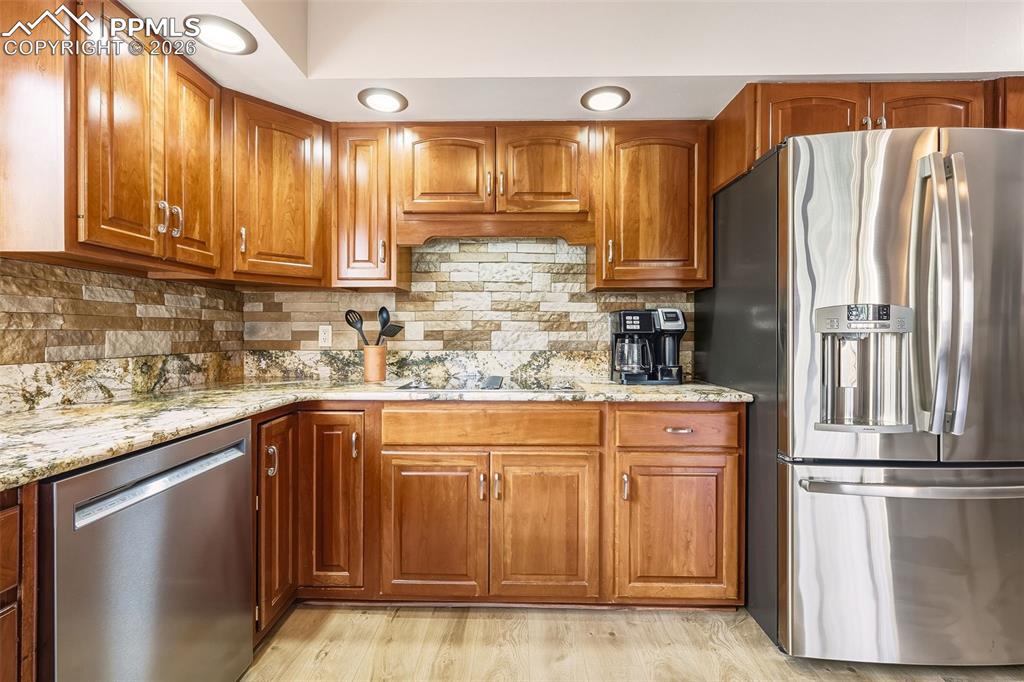 Warm wood cabinetry pairs beautifully with granite countertops and a stacked stone backsplash, complemented by stainless steel appliances and recessed lighting.