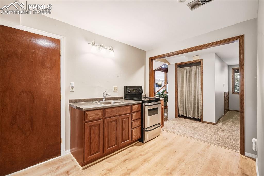 Lower-level kitchenette with sink, range, cabinetry, and updated flooring — includes designated space for a refrigerator, ideal for guest use, multigenerational living, or extended stays