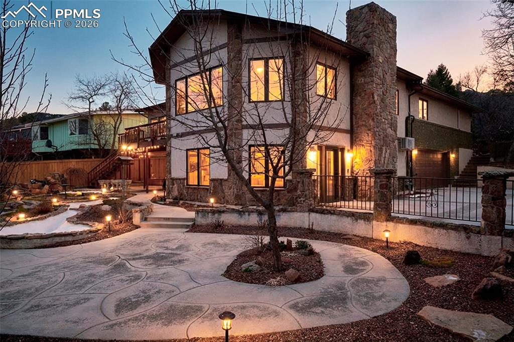 Architectural stone accents and expansive windows create a warm glow at dusk, showcasing the home’s walkout design and private backyard setting.