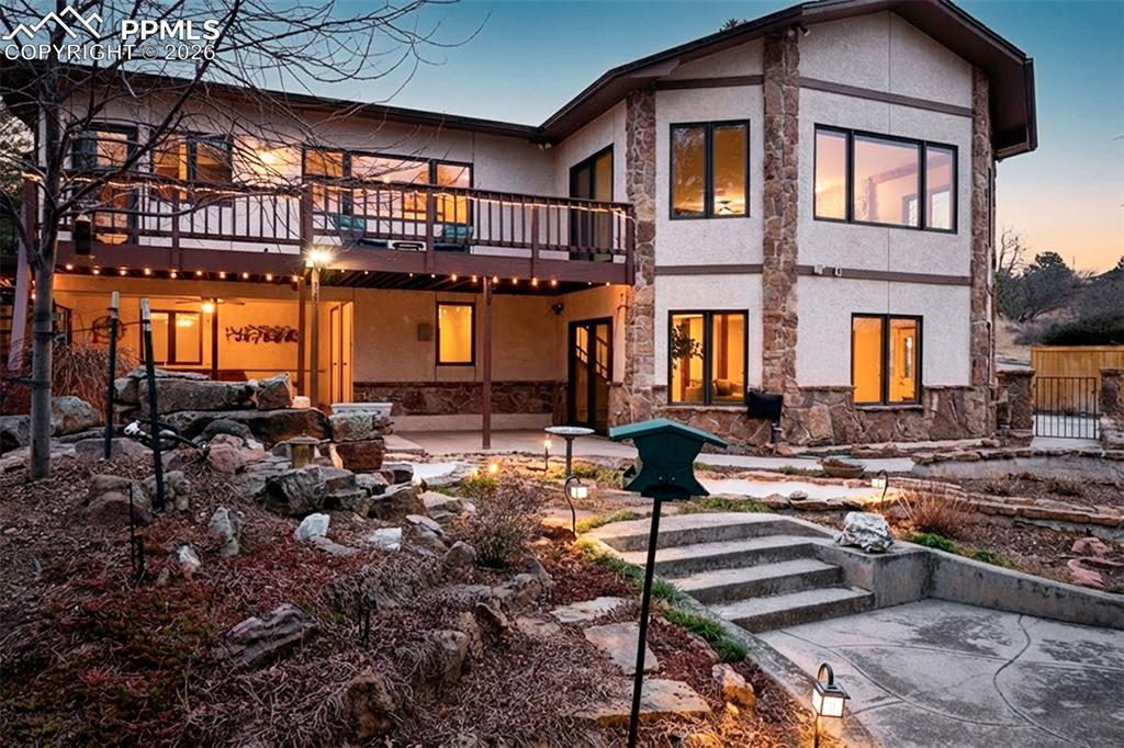 Stunning evening ambiance highlights the multi-level outdoor living spaces, upper deck, and covered patio below. Landscape lighting enhances both functionality and atmosphere.