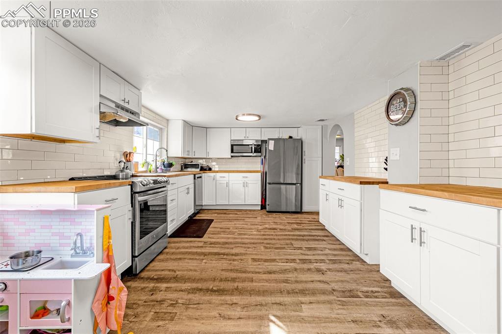 Kitchen with wooden counters, decorative backsplash, white cabinetry, and stainless steel appliances