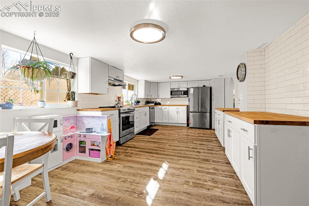 Kitchen featuring wooden counters, backsplash, stainless steel appliances, and light wood-type flooring