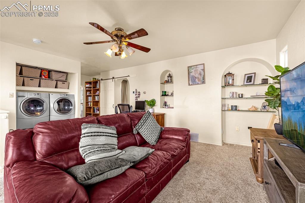 Carpeted living room with ceiling fan, washing machine and clothes dryer, and a barn door