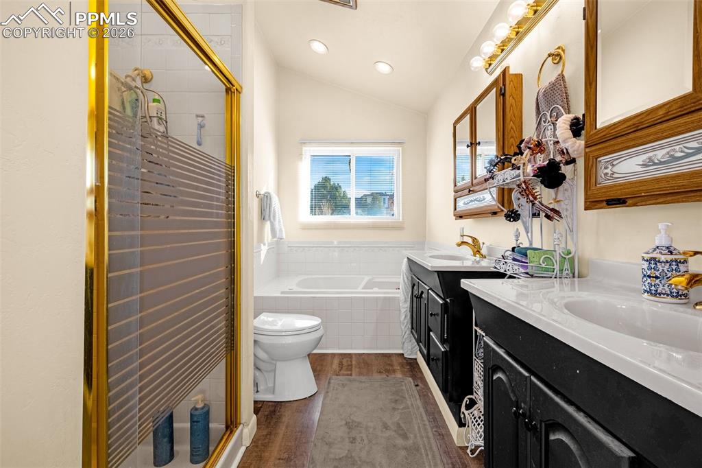 Bathroom featuring vaulted ceiling, dark wood-type flooring, two vanities, a bath, and a stall shower
