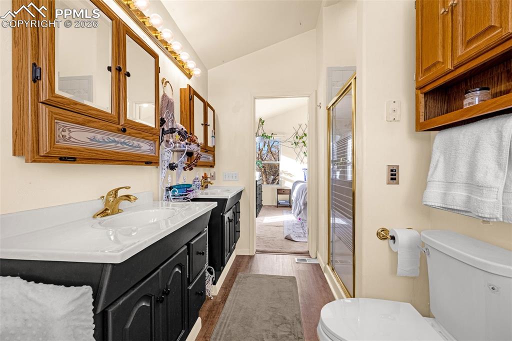 Full bathroom featuring vaulted ceiling, two vanities, a stall shower, dark wood finished floors, and ensuite bathroom
