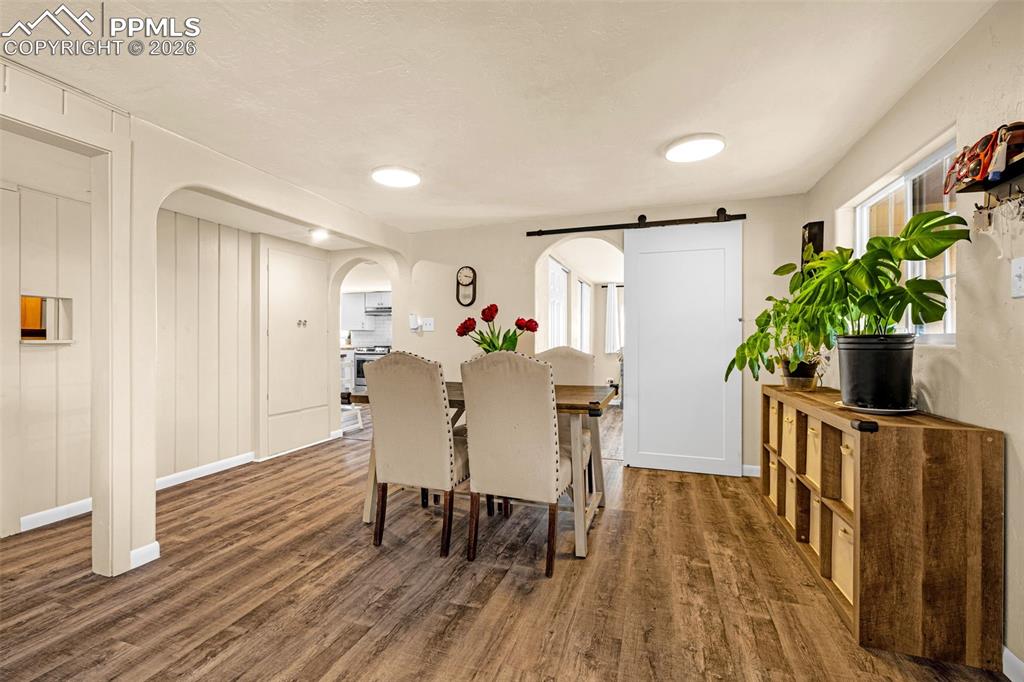 Dining area with arched walkways, dark wood-style floors, plenty of natural light, and a barn door