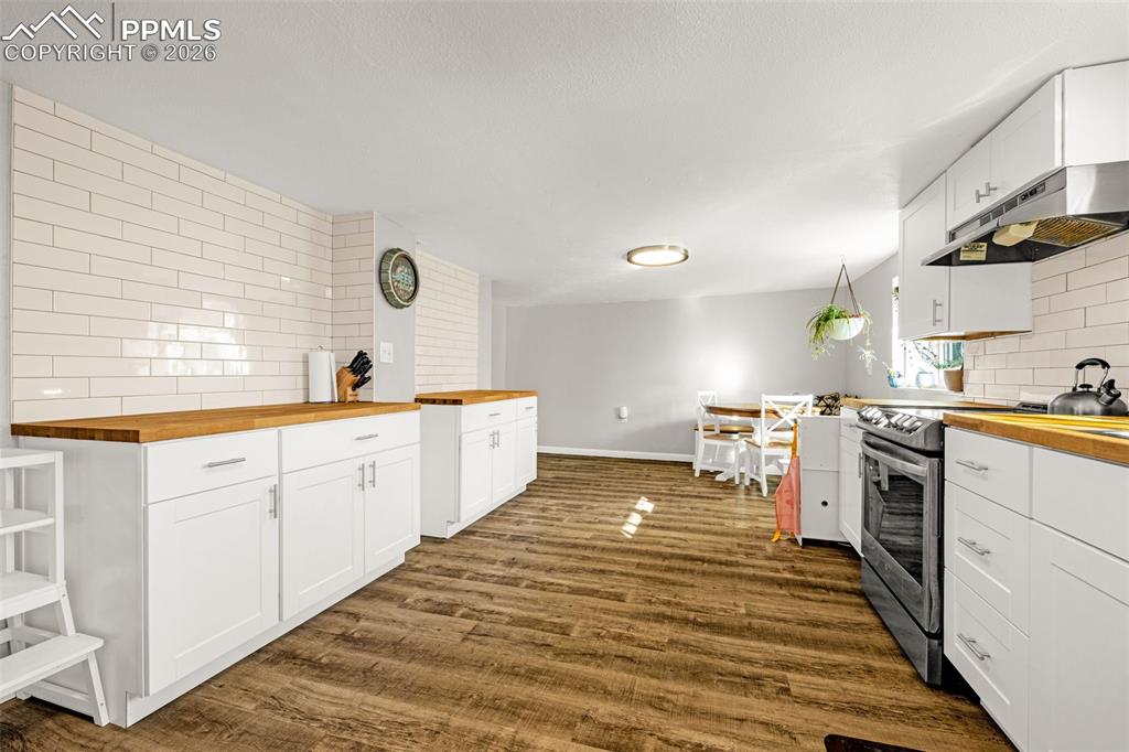 Kitchen with wooden counters, tasteful backsplash, electric stove, and white cabinets