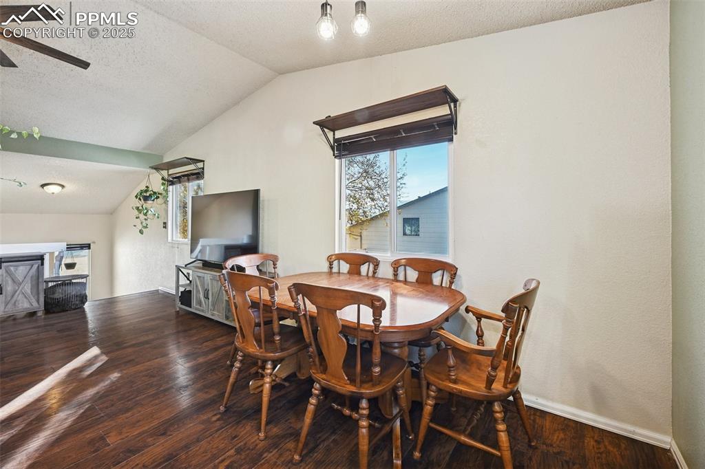 Dining room featuring a textured ceiling, dark wood finished floors, vaulted ceiling, and ceiling fan