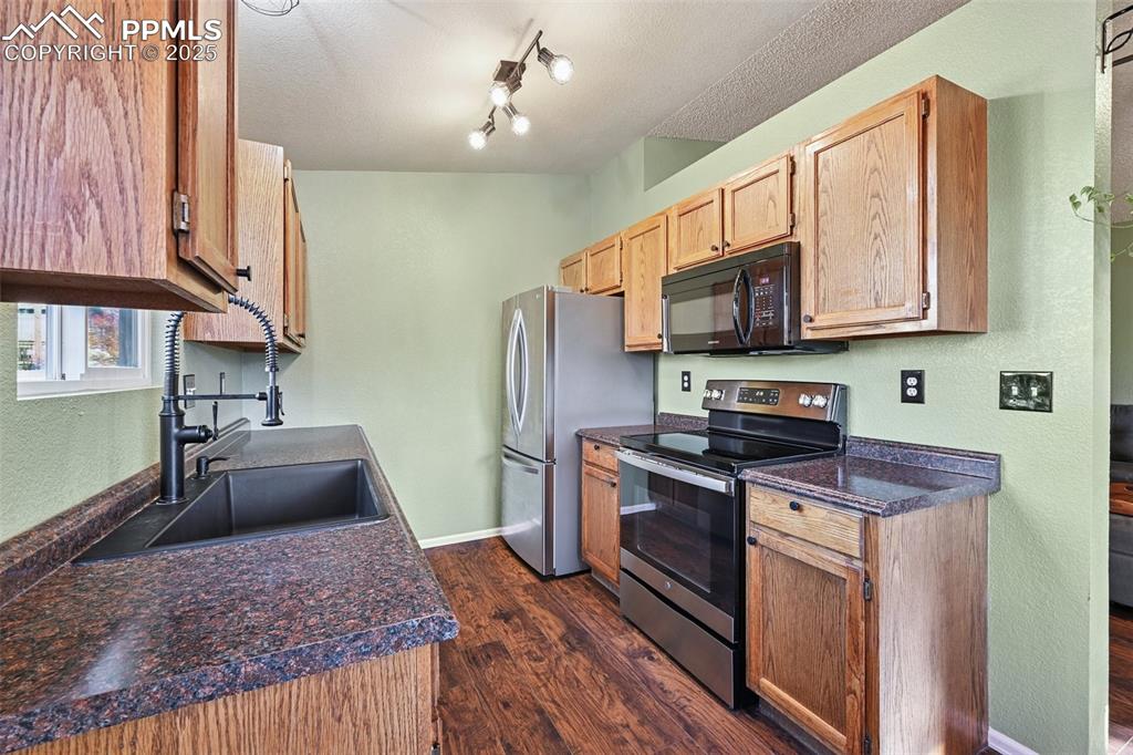 Kitchen with dark countertops, stainless steel electric range oven, dark wood-type flooring, a textured ceiling, and a textured wall