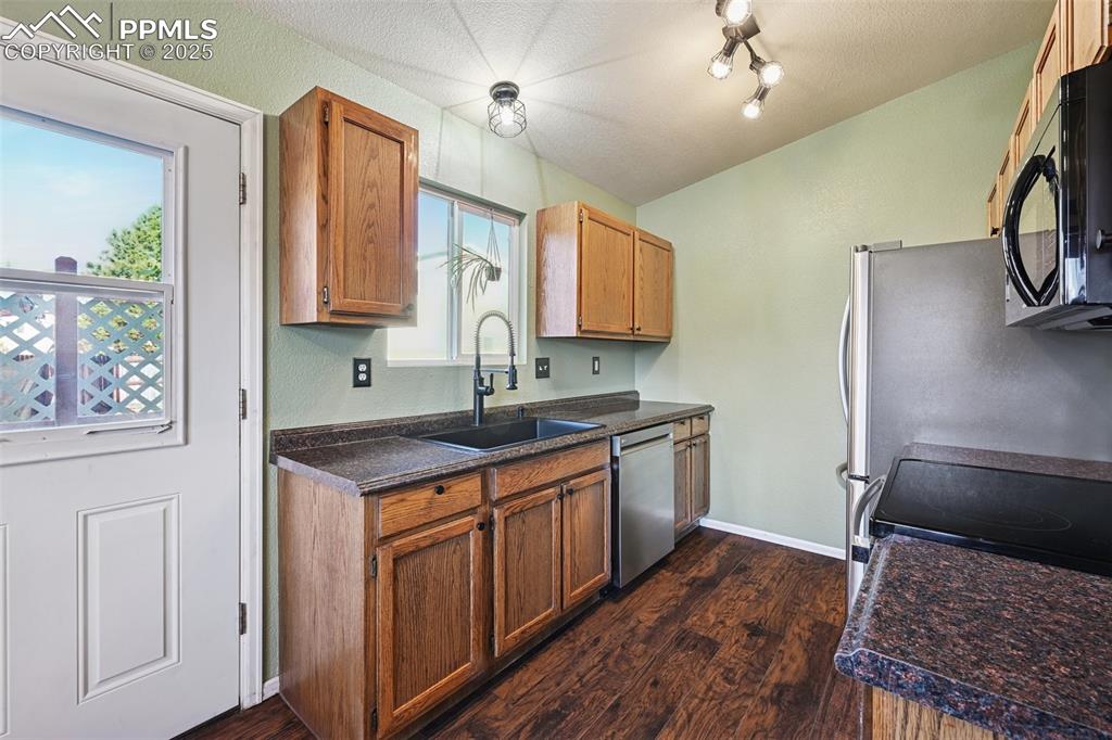 Kitchen with dark countertops, black appliances, dark wood-style floors, brown cabinetry, and a textured ceiling