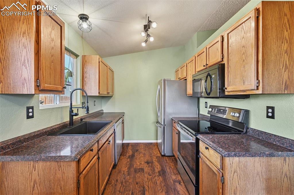 Kitchen featuring appliances with stainless steel finishes, dark countertops, dark wood finished floors, a textured ceiling, and a textured wall