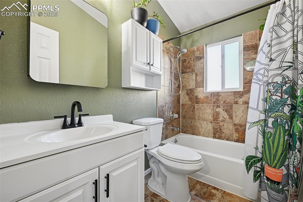 Full bath with a textured wall, shower / bath combo with shower curtain, and vanity