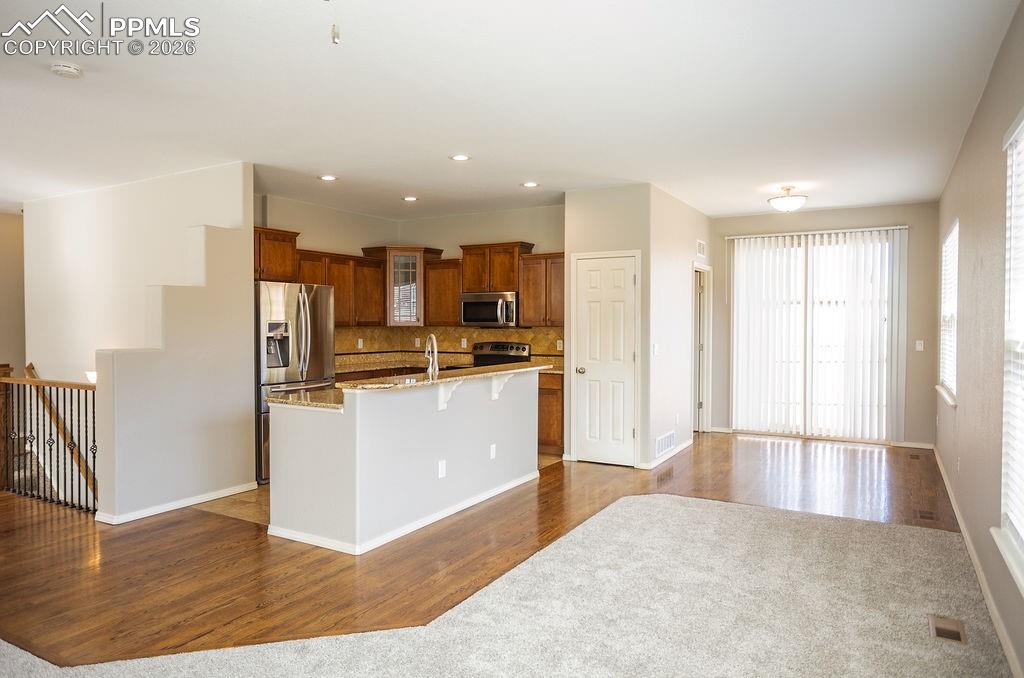 Kitchen featuring dark wood-type flooring, light stone countertops, stainless steel appliances, a kitchen breakfast bar, and wood finish cabinetry