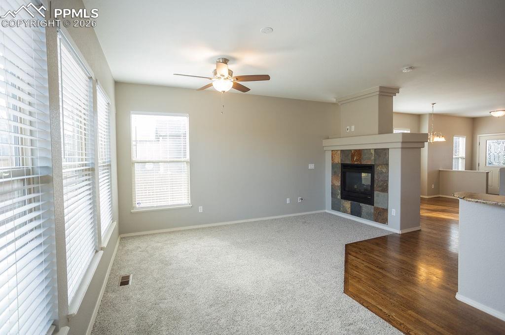 Unfurnished living room featuring carpet, a tiled fireplace, ceiling fan, and wood finished floors