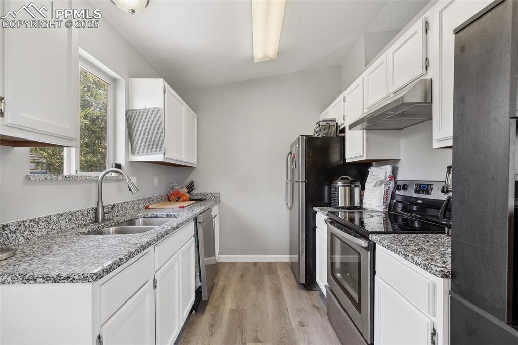 Kitchen with appliances with stainless steel finishes, under cabinet range hood, light wood-type flooring, and white cabinets