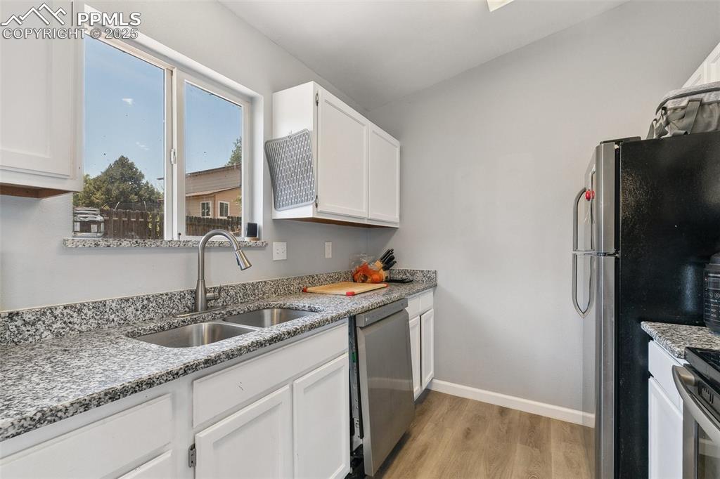 Kitchen with appliances with stainless steel finishes, light wood-style floors, white cabinets, and light stone countertops