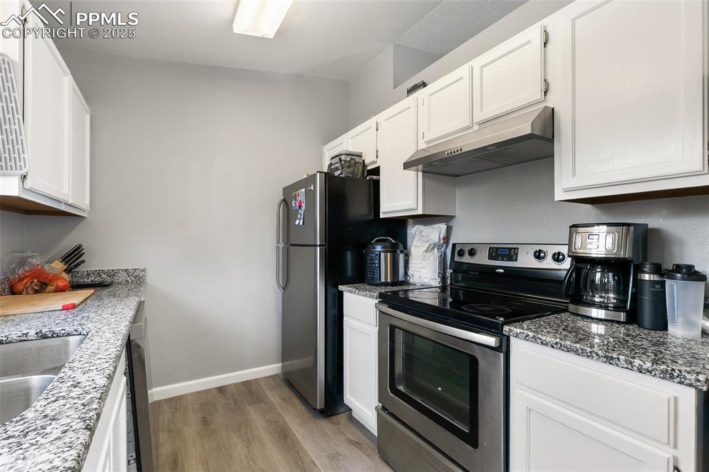 Kitchen with appliances with stainless steel finishes, under cabinet range hood, light wood-style flooring, and white cabinets