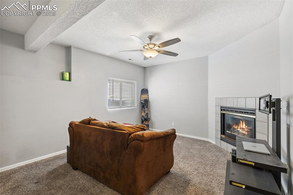 Carpeted living area with ceiling fan, a fireplace, and a textured ceiling