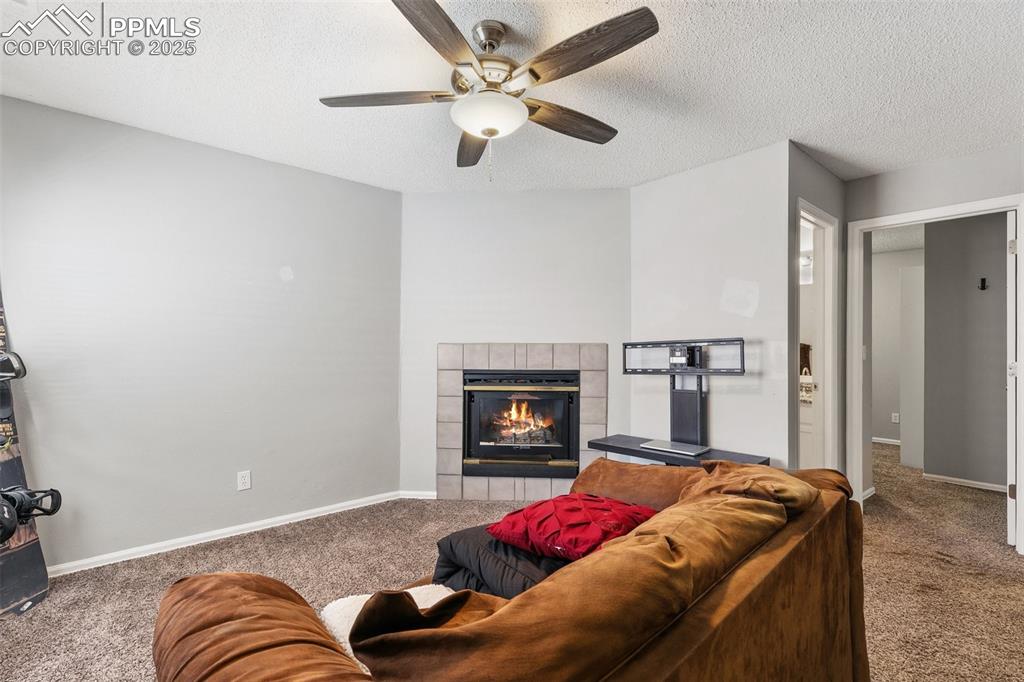 Carpeted living area with a fireplace, a ceiling fan, and a textured ceiling
