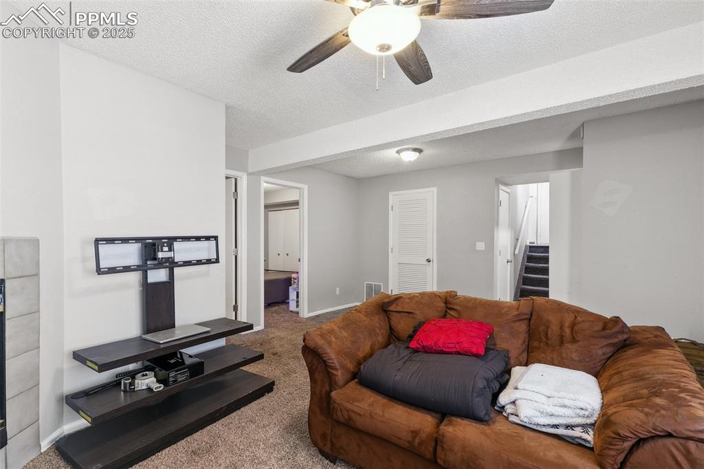 Carpeted living room with stairs, ceiling fan, and a textured ceiling